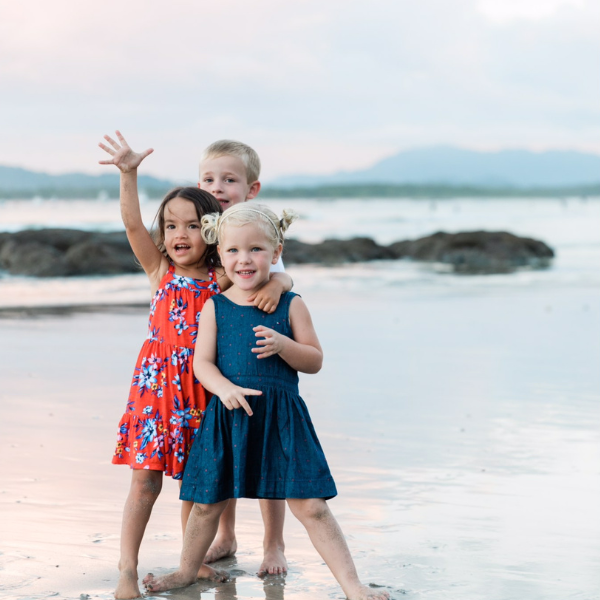  children on the beach waving and smiling at the camera