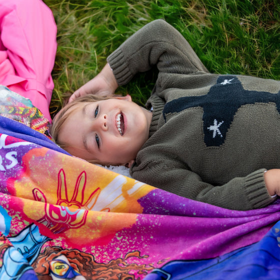 child laying out with the fleece superhero blanket on the grass